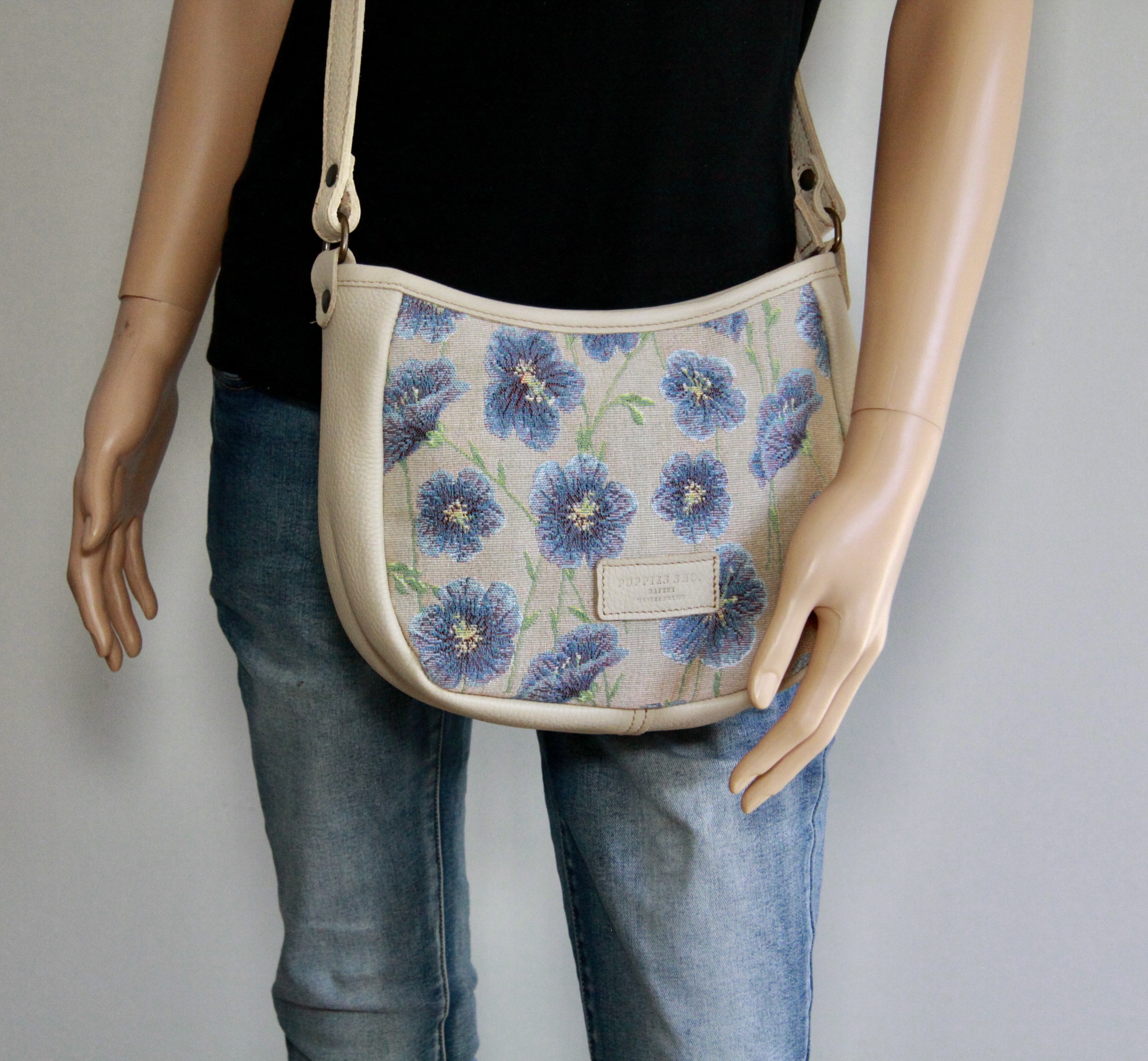 Sac à main en tissu jacquard aux motifs floraux, porté par un mannequin contre un fond neutre.
