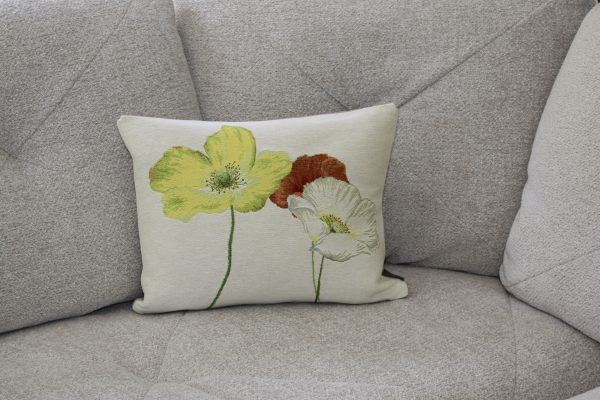 Coussin décoratif avec des coquelicots brodés sur fond clair, posé sur un canapé gris.
