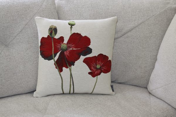 Coussin décoratif beige avec broderie de coquelicots rouges, posé sur un canapé.