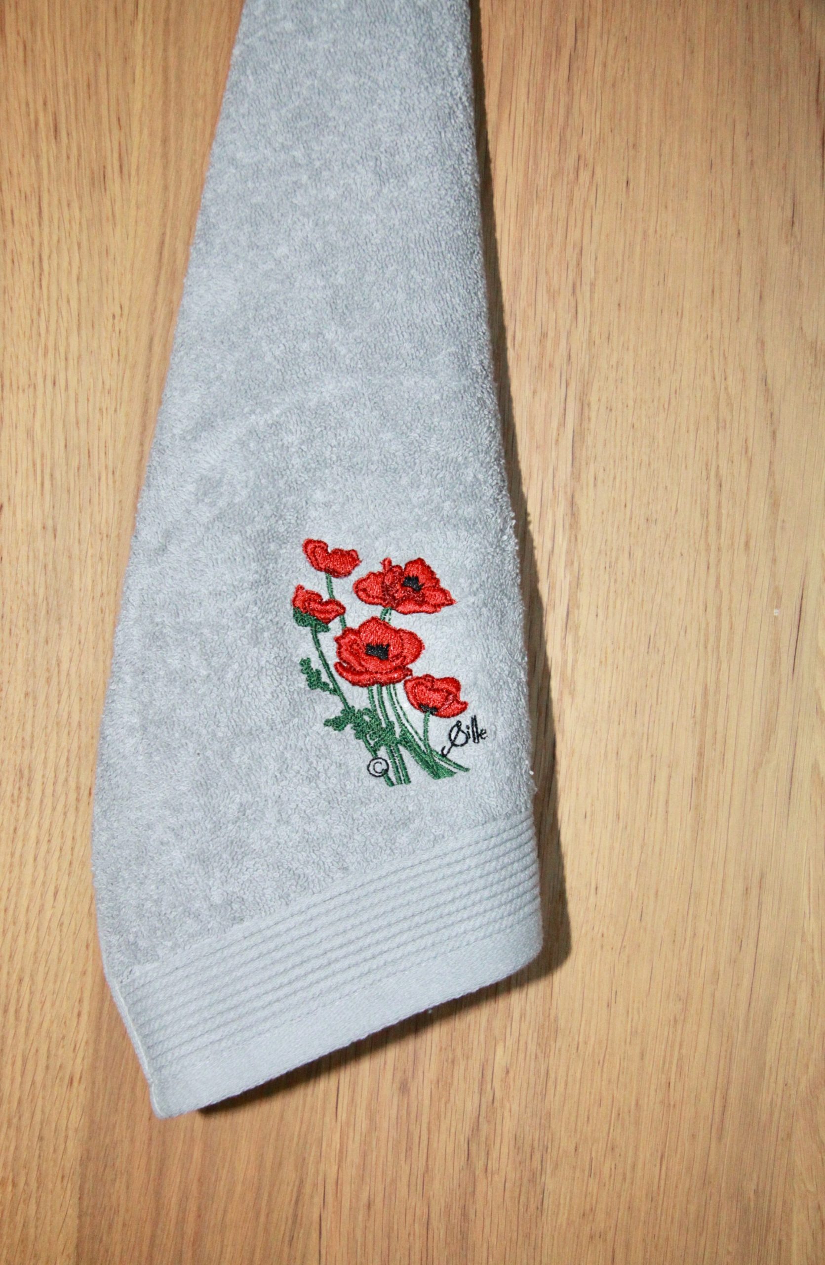 Serviette grise avec broderie de coquelicots rouges, design artistique de Sqille, fabriquée en France.