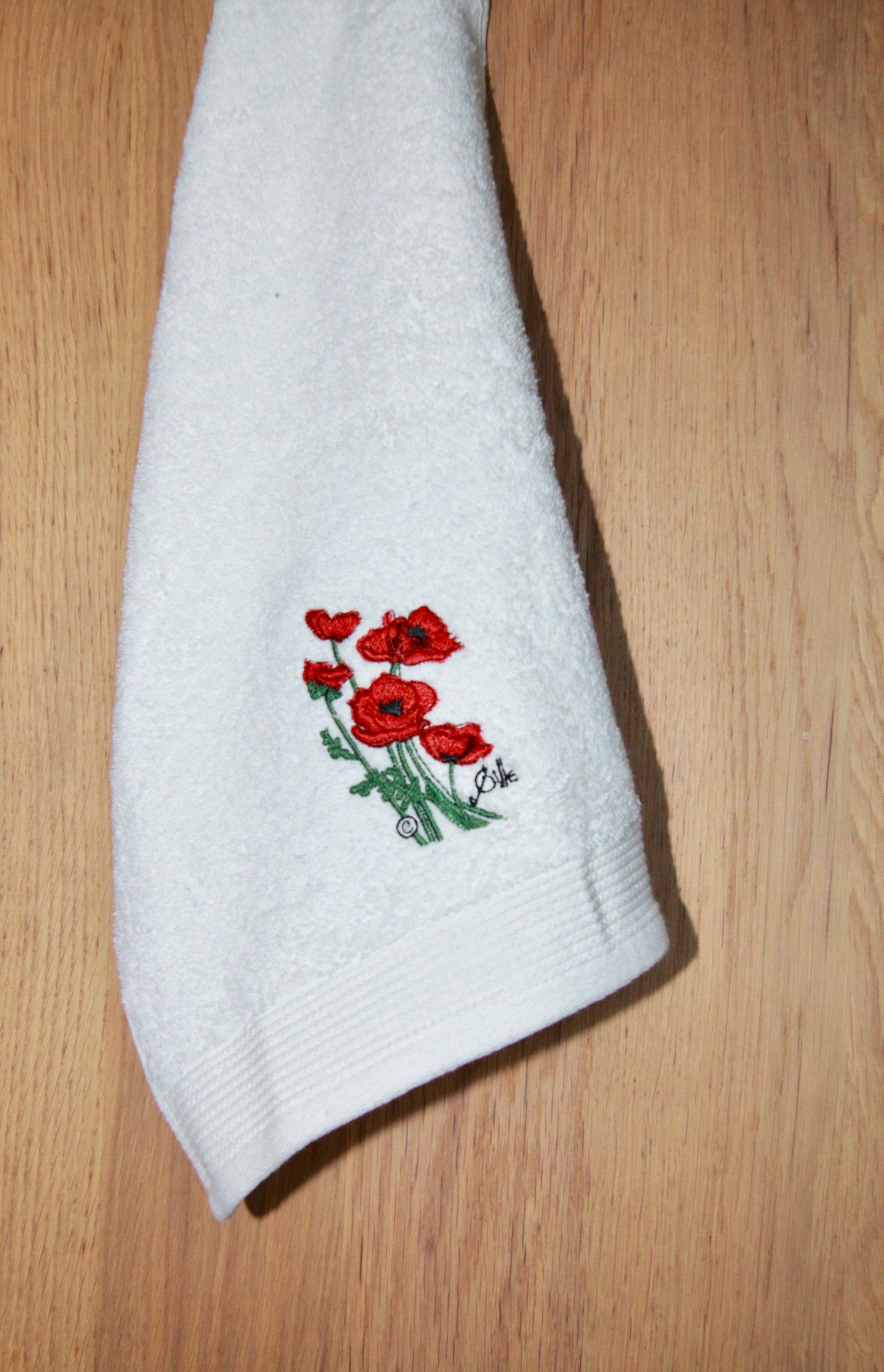 Serviette blanche avec broderie de coquelicots rouges, provenant de Poppies Shop à Bayeux, spécialité floral et artisanat français.
