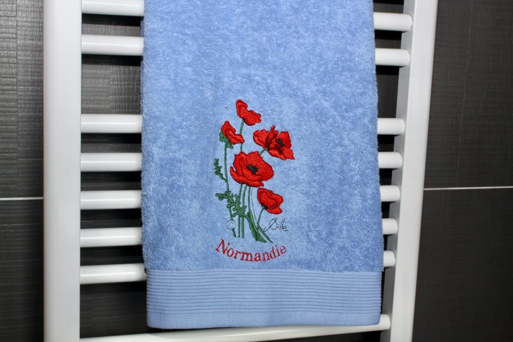 Serviette de toilette bleue avec broderie de coquelicots et inscription "Normandie".