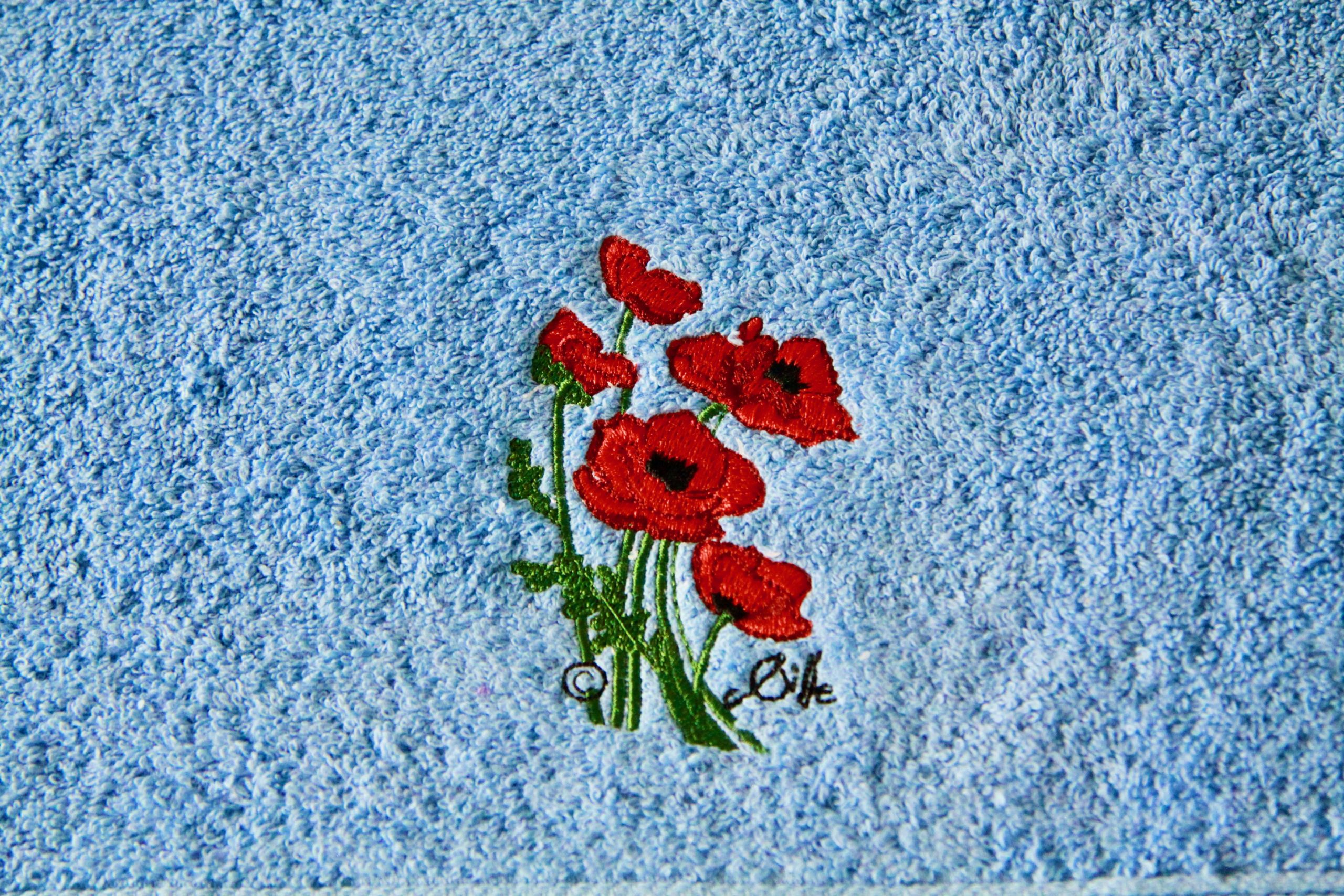 Blue bath towel with red poppy embroidery, made by Poppies Shop, an artist's shop in Bayeux.