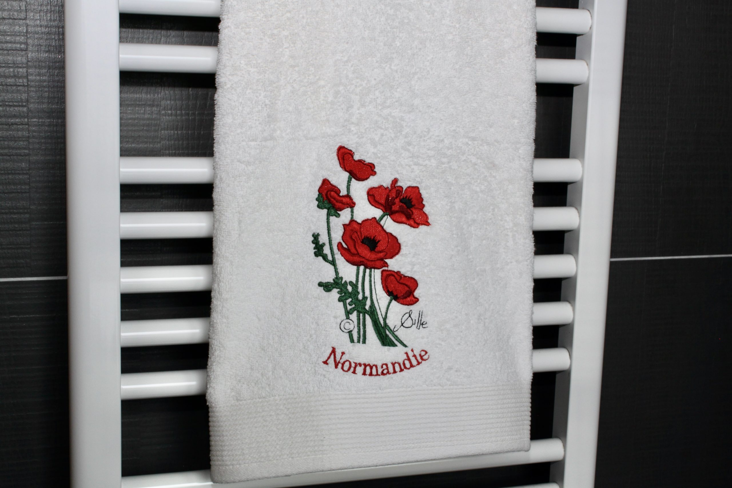 White bath towel embroidered with red poppies and the word "Normandy".