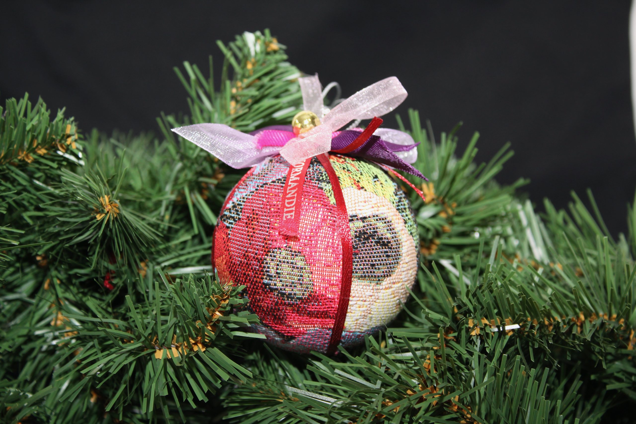 Boule de Noël en tissu avec motifs floraux, décorée de rubans, accrochée à une branche de sapin.