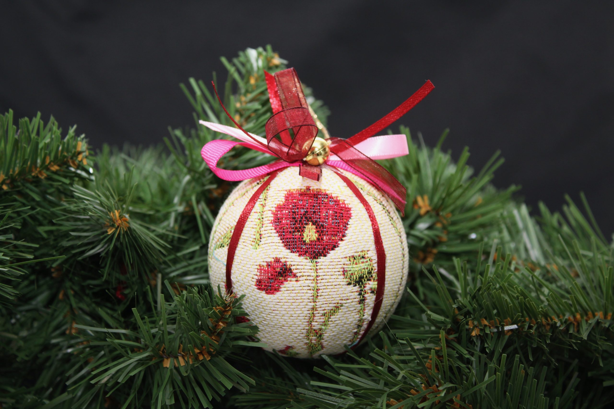 Boule de Noël en tissu avec motifs de coquelicot, décorée de rubans, reposant sur des branches de sapin.