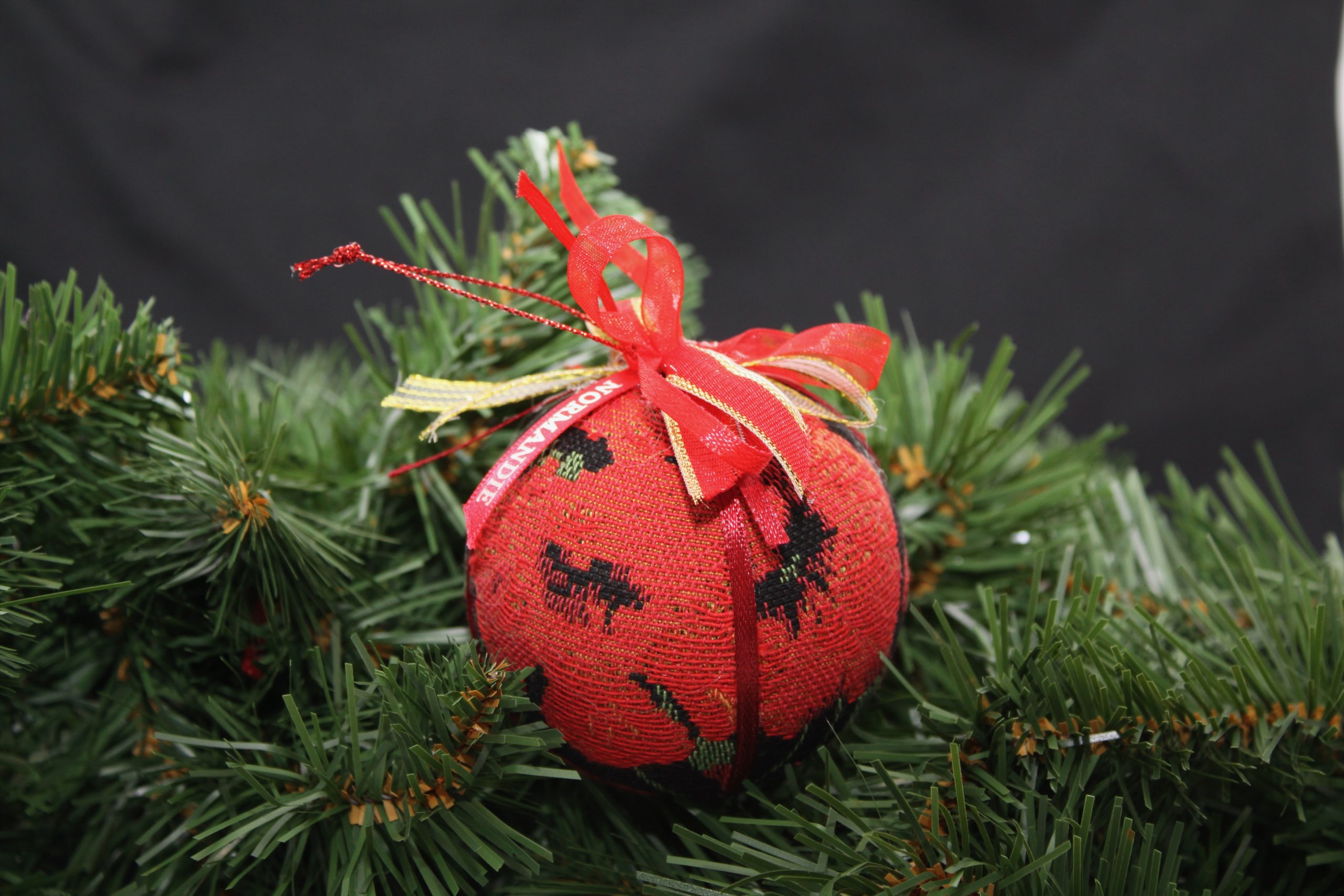 Boule de Noël en tissu rouge ornée de coquelicots, décorée de rubans, posée sur des branches de sapin.
