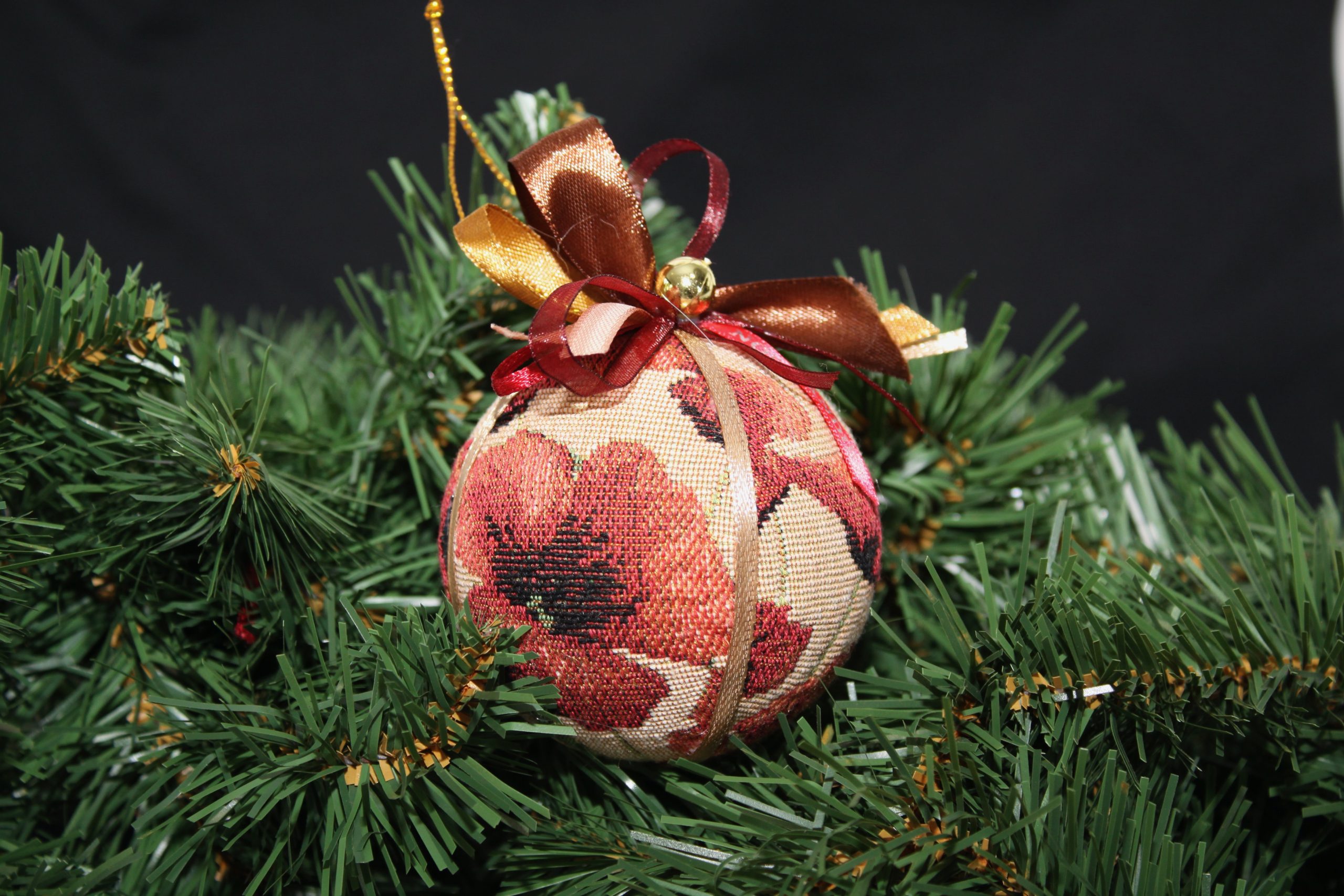 Boule de Noël en tissu jacquard avec motif coquelicot, ornée de rubans, accrochée à un sapin.