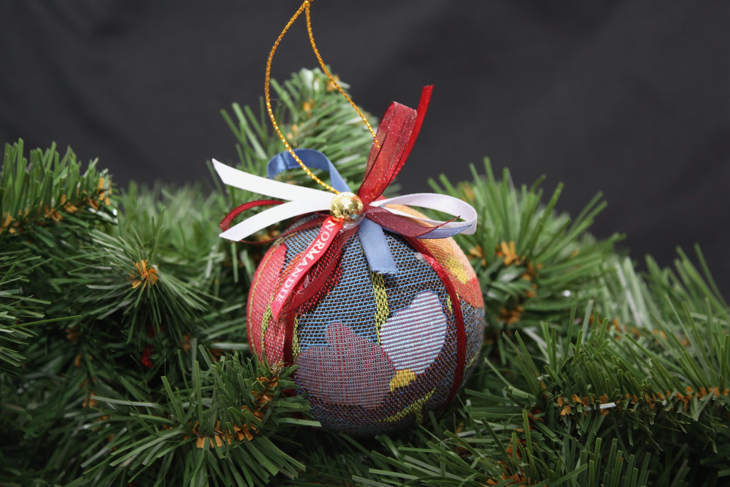 Boule de Noël en tissu jacquard avec motifs floraux, décorée de rubans, suspendue à un sapin.