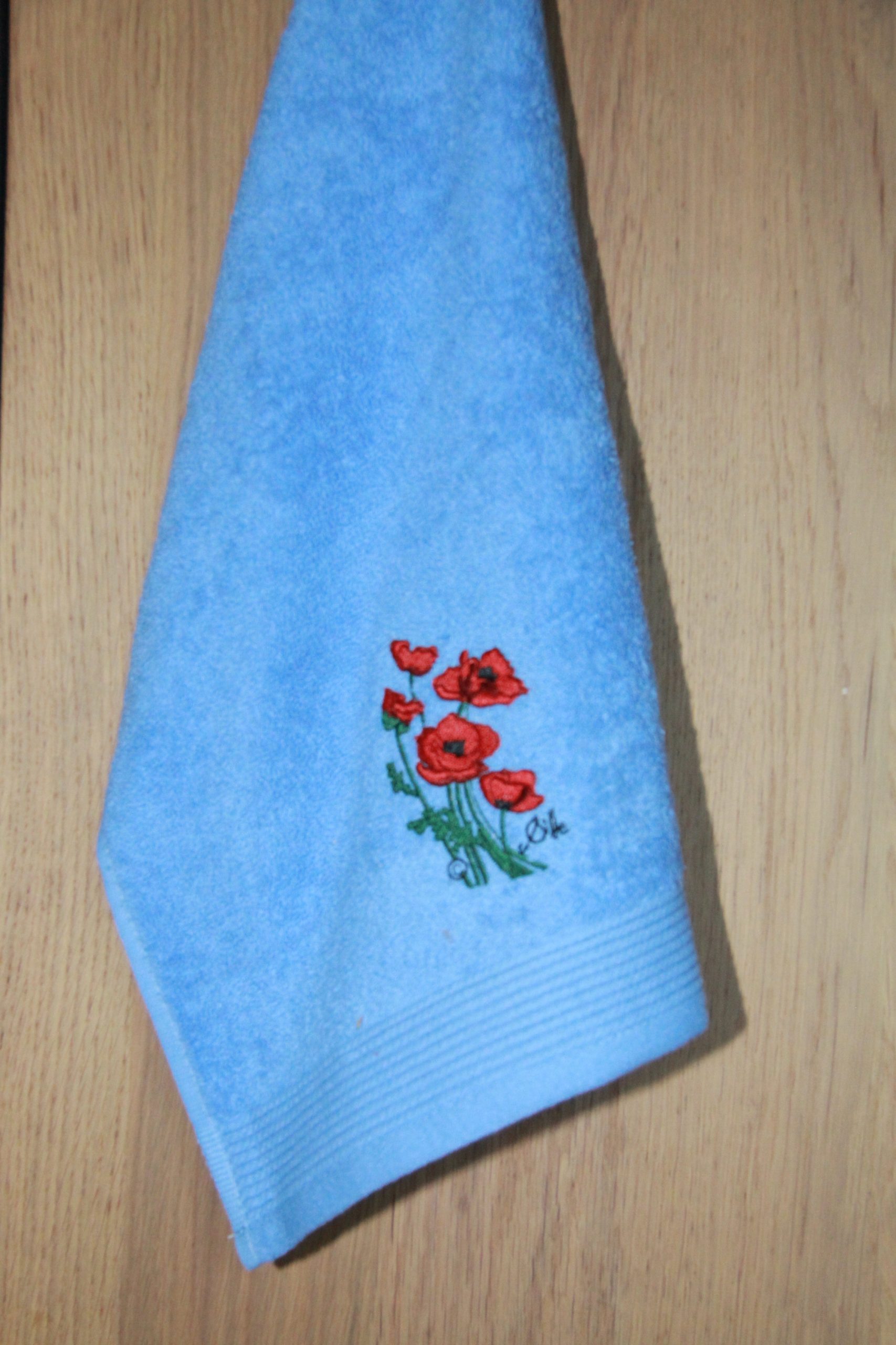 Serviette invité bleue avec broderie de coquelicots, fabriquée en France, reflet du style floral de Poppies Shop à Bayeux.