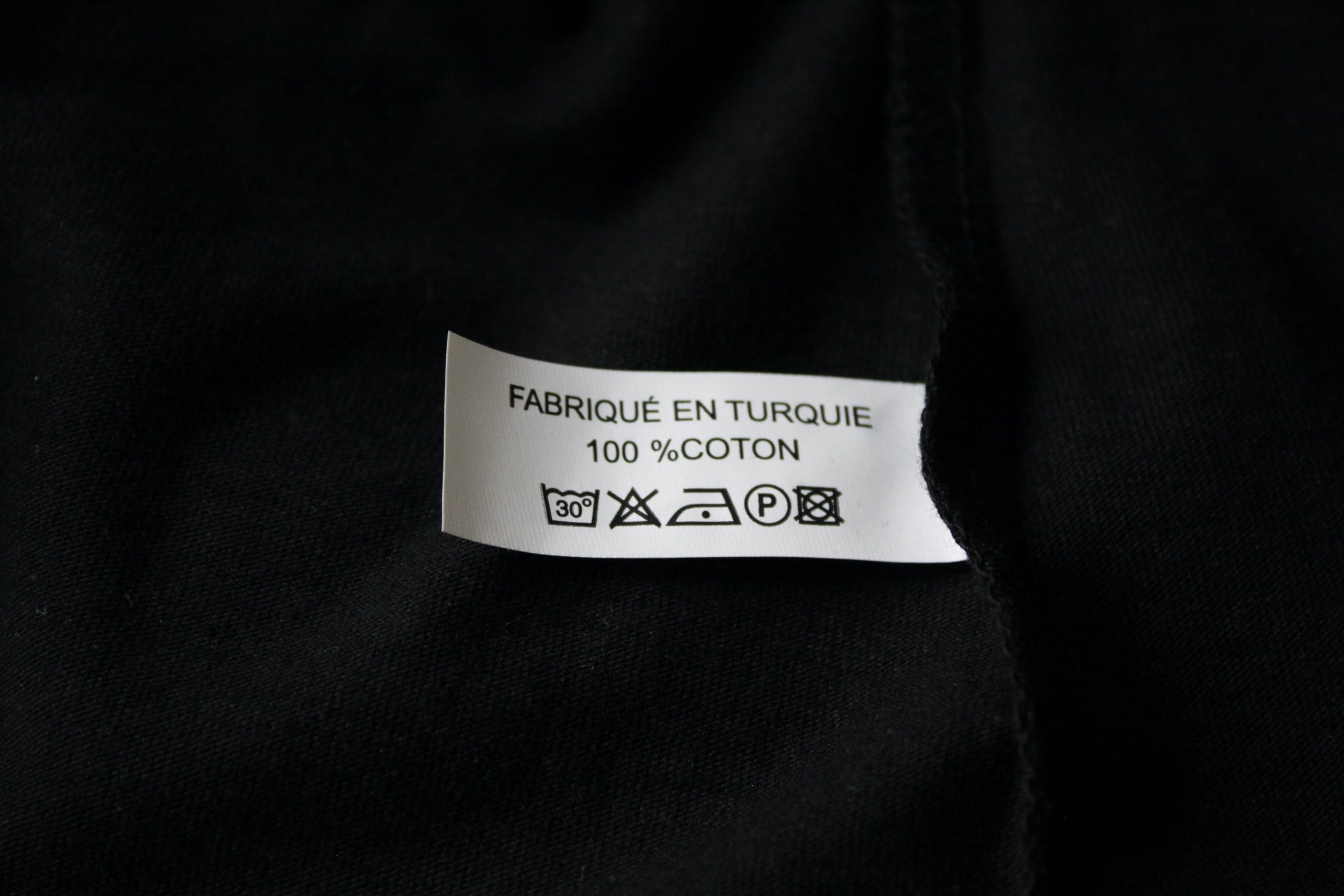Étiquette d'un T-shirt noir indiquant "Fabriqué en Turquie, 100 % coton".